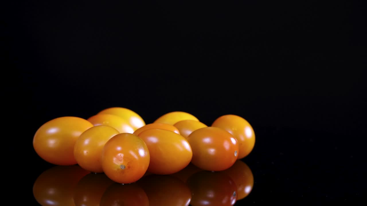 Cherry tomatoes rotate on a glossy black surface under bright lighting, creating a dynamic visual effect