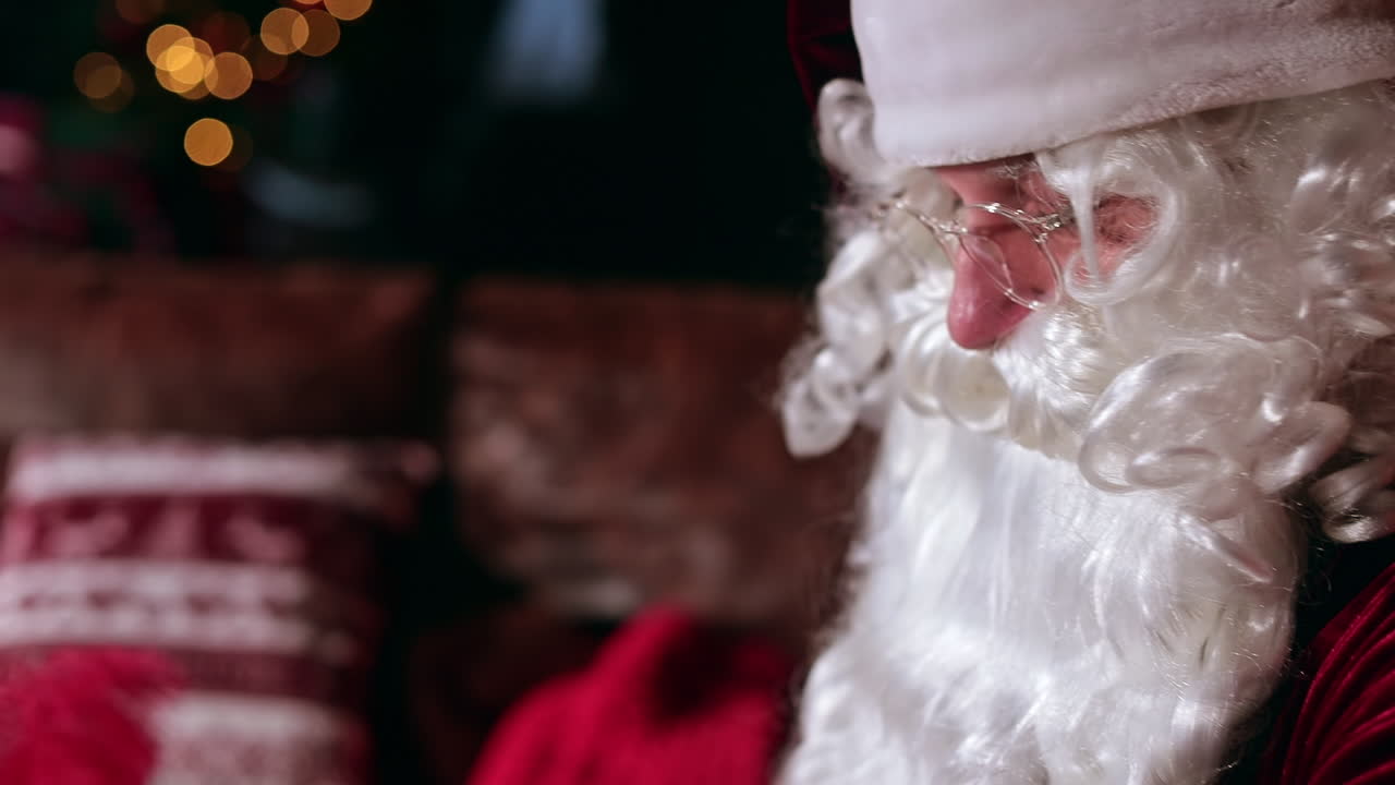 Santa Claus sitting indoors busy with his things. Close up portrait of a famous personage sitting his side to the camera. Blurred backdrop.
