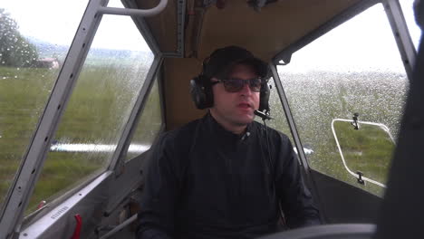 Static-close-up-FHD-shot-of-a-male-pilot-sitting-in-a-cockpit,-adjusting-his-headphone-set-and-waiting-for-a-sign-to-take-off-from-a-field-airport