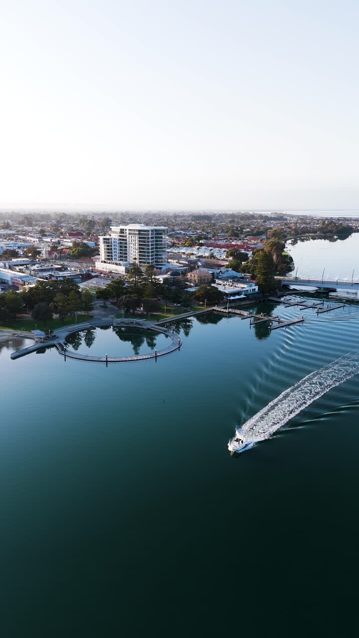 Mandurah foreshore at sunrise as a boat cruises through the water. Vertical tracking aerial shot