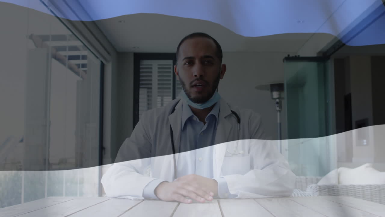 エストニアの国旗のアニメーションでマスクをかぶった男性医師がデスクでビデオコンサルティングを行っています