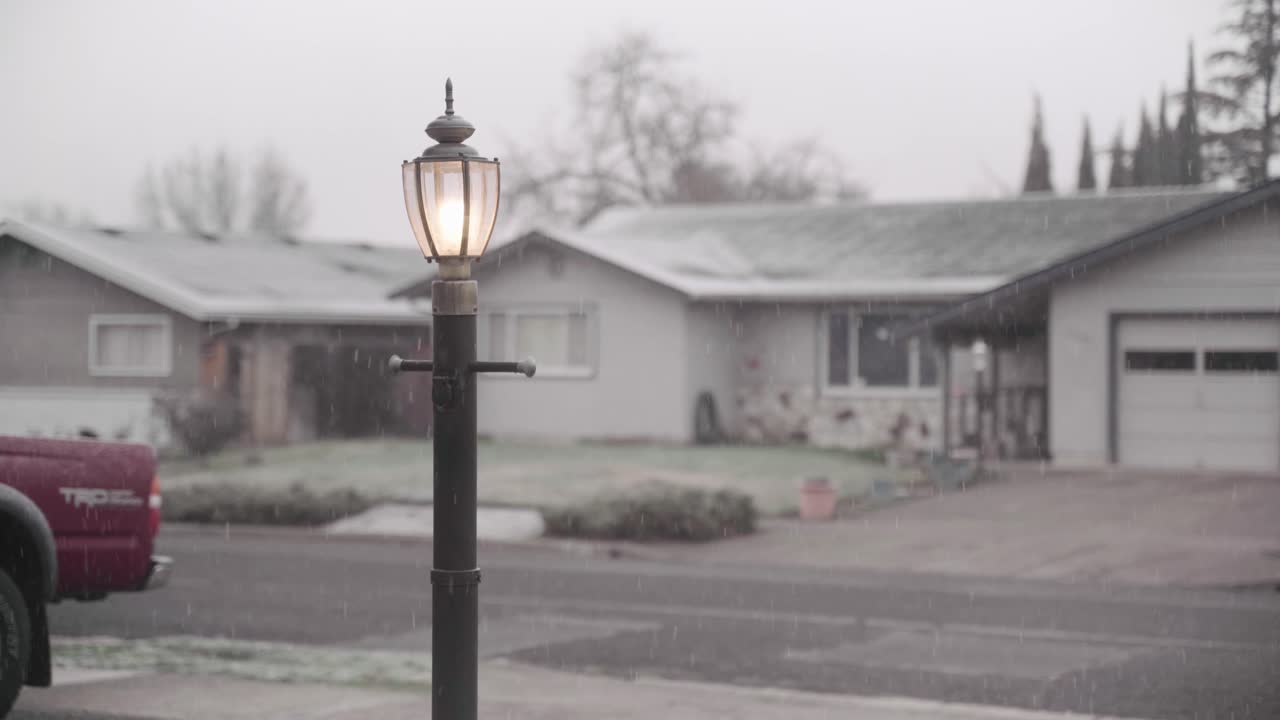 poste de luz con luz encendida en medio de una ligera nevada de un barrio suburbano | 4k