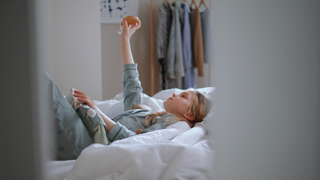 Child making sunny bunny reflecting mirror at morning bedroom. Girl lying bed
