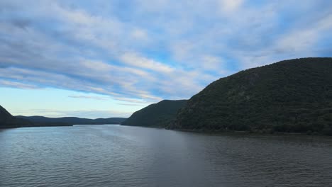 aerial drone footage rising over the hudson river in new york's hudson valley with storm king mountain in the background at susnet