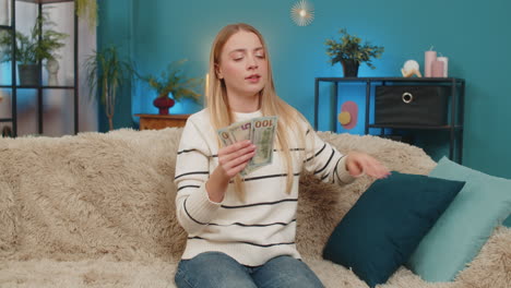 caucasian woman finding lost dollar cash on sofa counting money searching missing banknote indoors