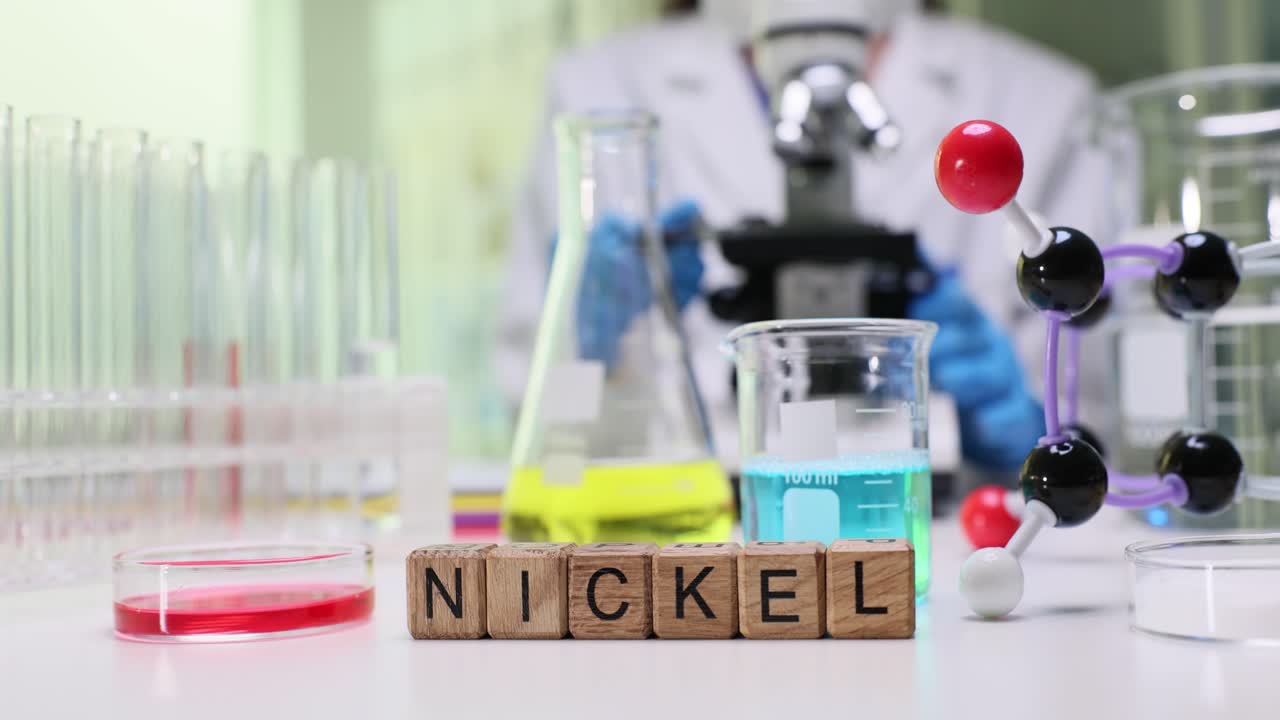 Wooden blocks spell nickel near beaker and molecule model