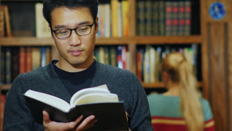 Gut-Aussehender-Asiatischer-Mann-Mit-Brille,-Der-Ein-Buch-In-Der-Bibliothek-Liest-1