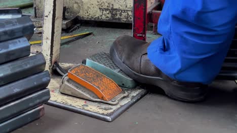 an operator's feet wearing safety shoes are stepping on the pedal of the machine to operate it