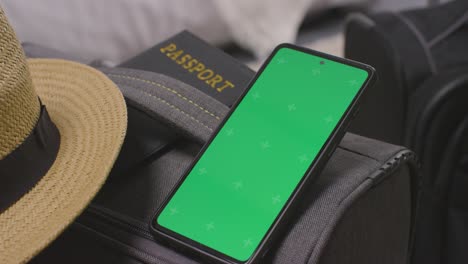 hat passport and green screen mobile phone on suitcase at home packed and ready for summer holiday