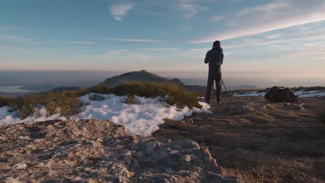 back view wide angle shot of young hiker taking photos with his camera and trípod on summit of snowy mountain in guadarrama mountains, madrid, spain