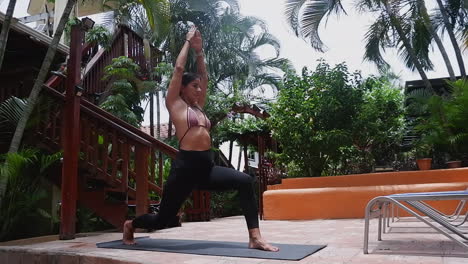 young woman on tropical back deck progresses through warrior yoga pose