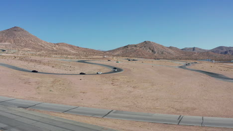 Cars-race-for-the-championship-at-a-racetrack-with-the-Mojave-Desert-landscape-as-a-backdrop---aerial-view