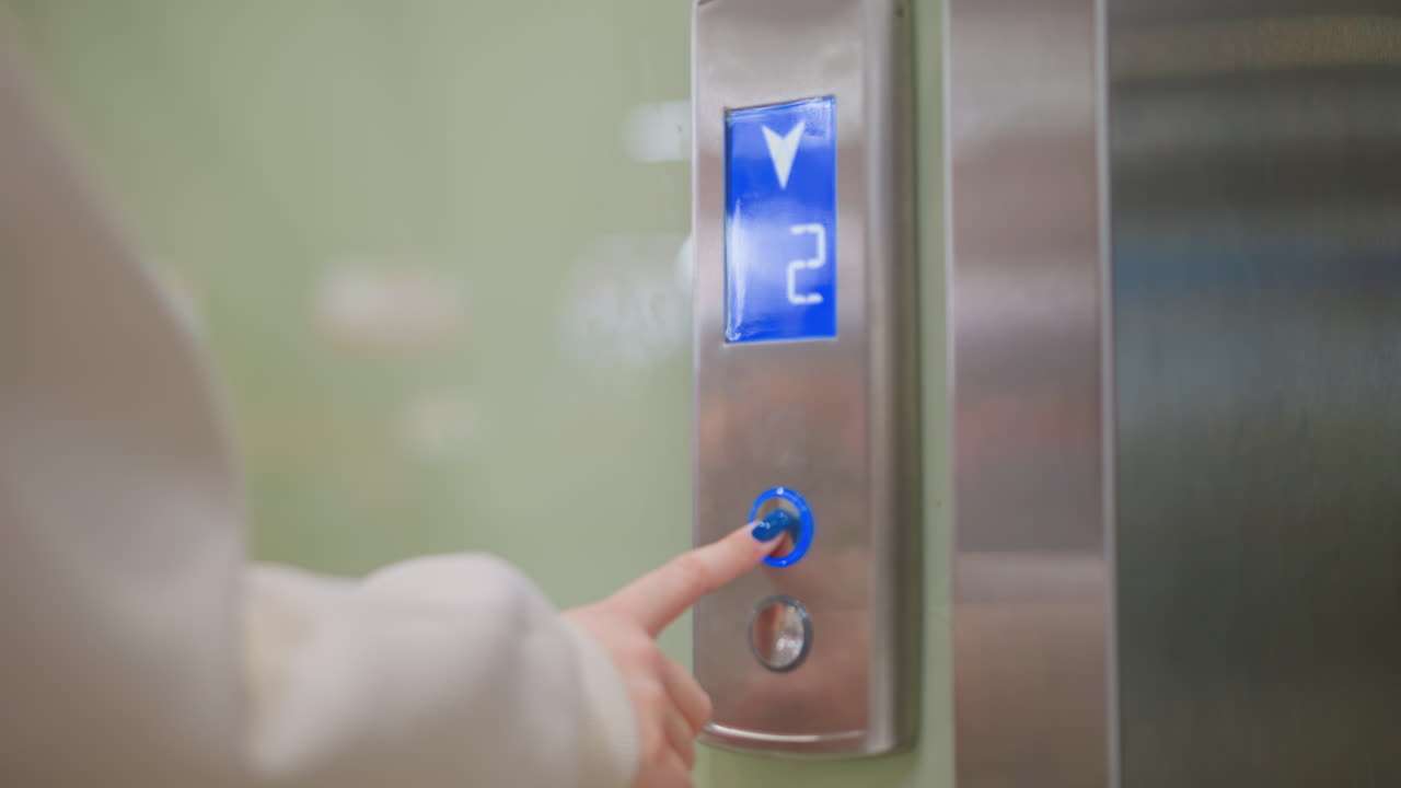 Close up hand of young woman with blue polished nails pressing elevator button to call lift, illuminated display showing floor number two, modern interior creating realistic everyday urban lifestyle
