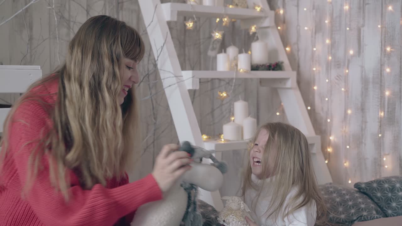 아름다운 금발 여성이 침대에서 작은 귀여운 소녀와 놀고 있습니다.