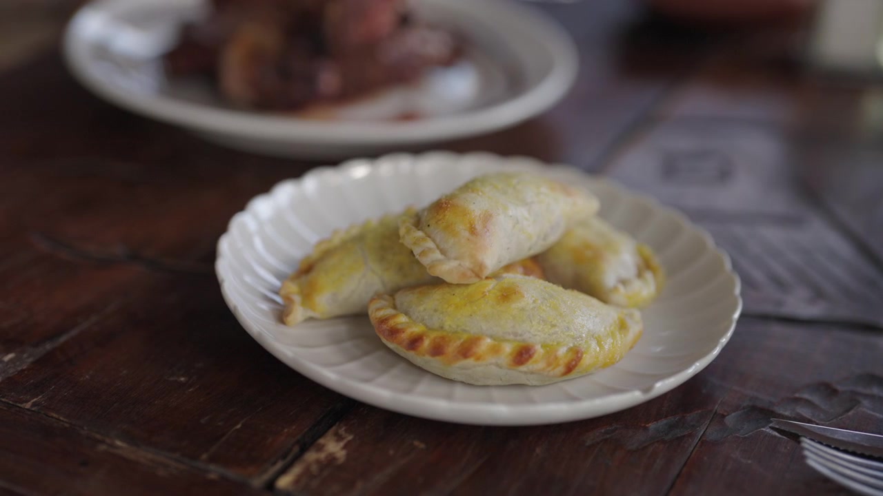 Un primo piano di empanadas argentine appena sfornate su un piatto bianco, posizionato su un tavolo di legno rustico. Ideale per blog di cucina o presentazioni culinarie