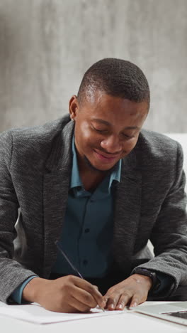 smiling african-american guy student writes notes listening to lecture via contemporary laptop at small low table at home slow motion