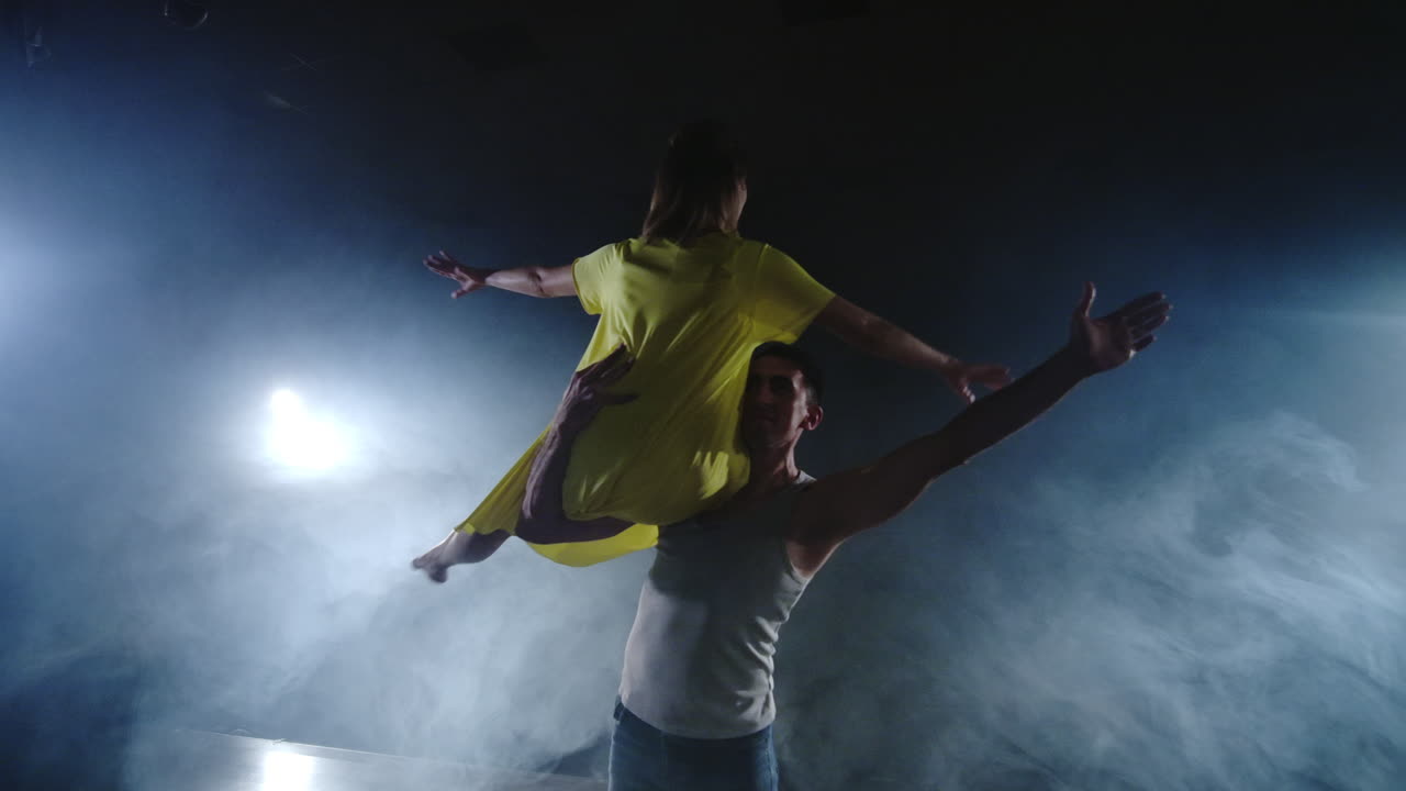 dos bailarines de ballet modernos están bailando en el escenario en el humo un hombre levanta a su pareja en sus brazos y gira en el aire. el musical utiliza bailarines acróbatas de circo.