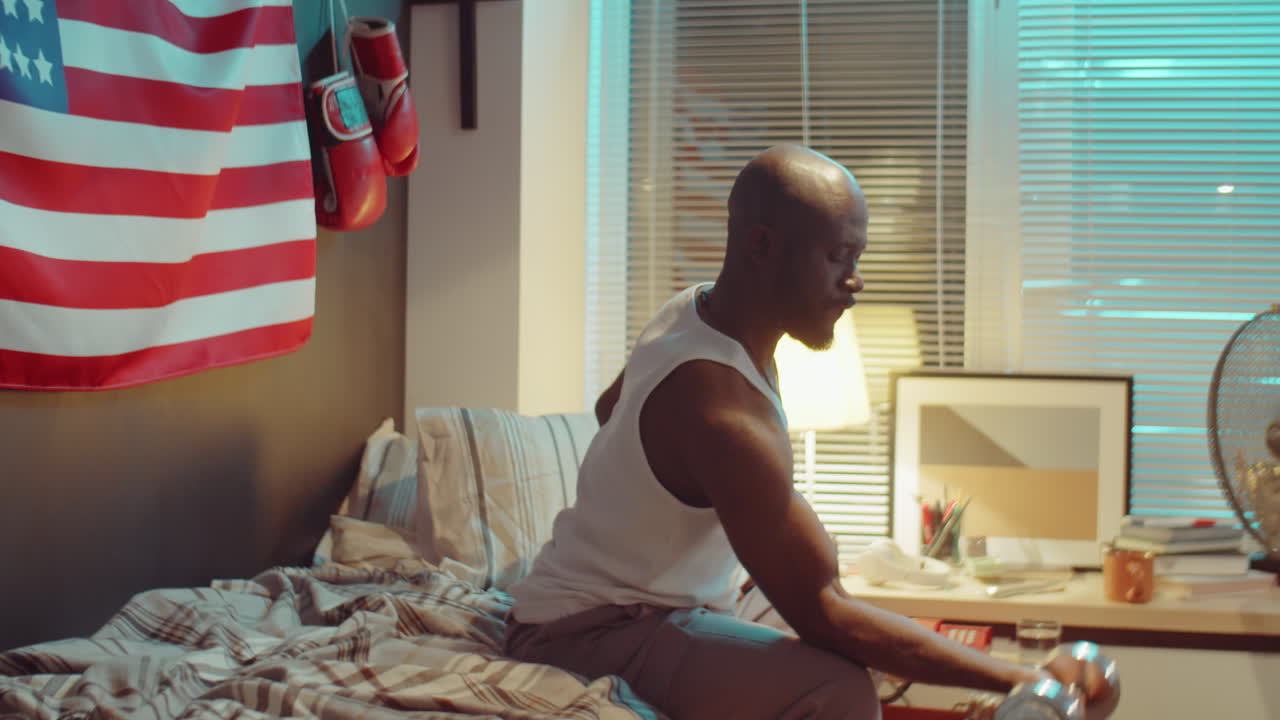 아프리카계 미국인 남자가 집에서 덤벨로 운동하고 있습니다.