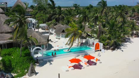 tourists relaxing in pool at luxury bohemian hotel on tropical white sand beach in tulum mexico, aerial