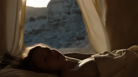 a woman sleeping peacefully in a tent as morning light illuminates the desert landscape outside