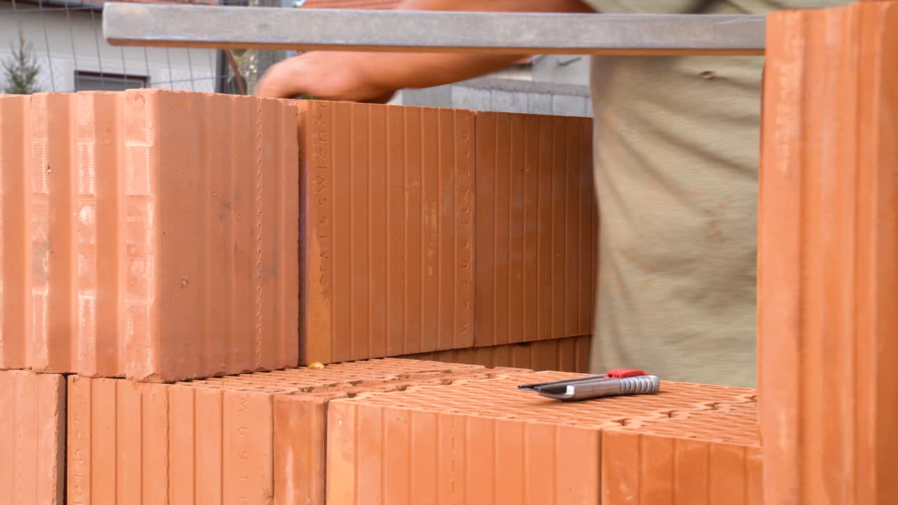 Worker laying ceramic brick into wall while using leveler tool