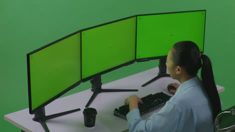 vista lateral de una mujer asiática con dolor de cabeza mientras trabaja con múltiples monitores de computadora simulados en un estudio de pantalla verde