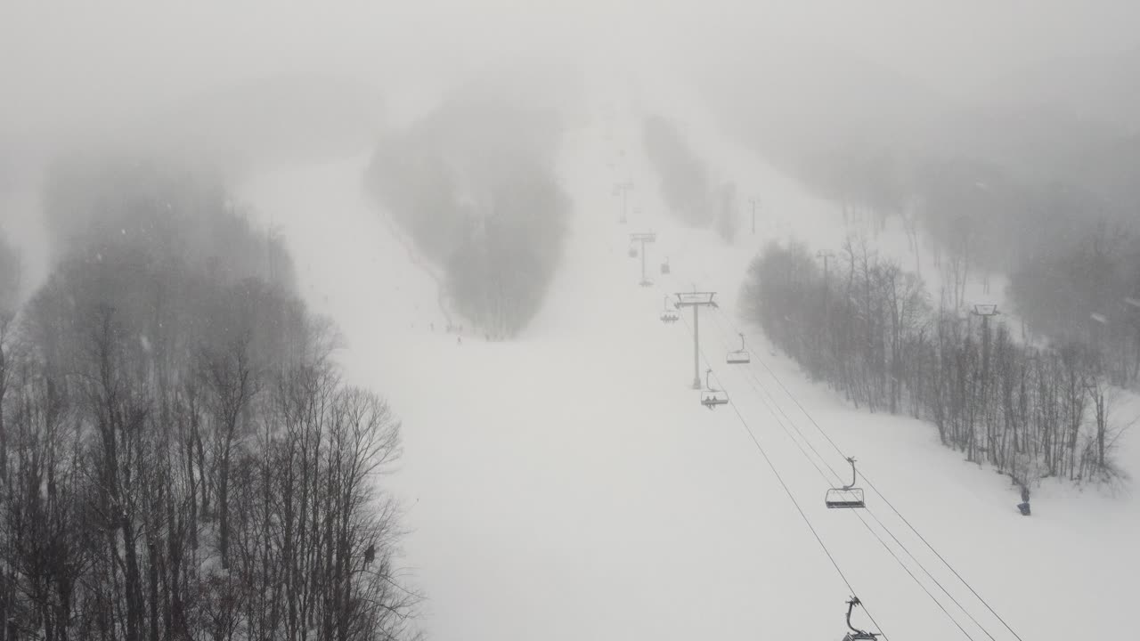 Foggy snow-covered ski resort with chairlift cables extending into the mist, Orford, Quebec, Canada.