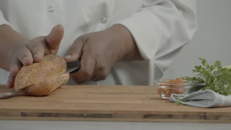 close up of chef's hand cutting bread. man cuts fresh bread with a knife on a wooden cutting board. breakfast or lunch concept