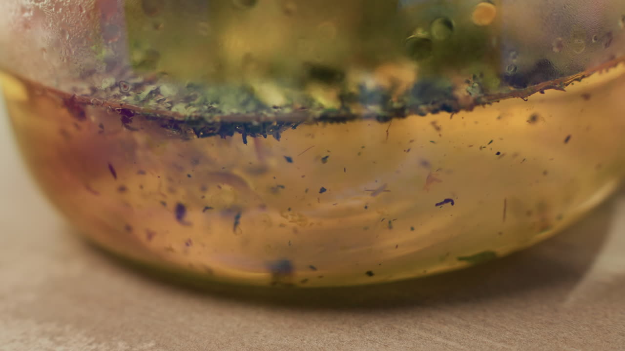 Botanik parçacıklı altın masaj yağı, mavi pigment benekleri içeren cam kavanozda viskoz jelin yakın çekimi, mikro akım terapisi için bitkisel infüzyon, sıcak ortam tonları, ideal dokunsal doku.