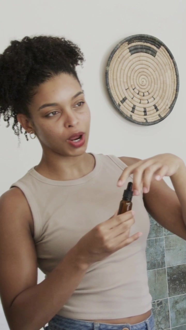 Vertical video: Raising bottle, woman showing and inspecting amber dropper in bathroom in beige top