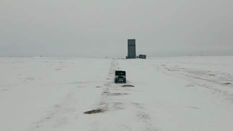 Aerial-of-UTV-driving-on-snow-covered-road-in-winter-across-open-field,-4K