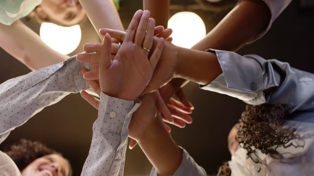 Low angle of happy diverse businesswomen stacking hands at office, in slow motion