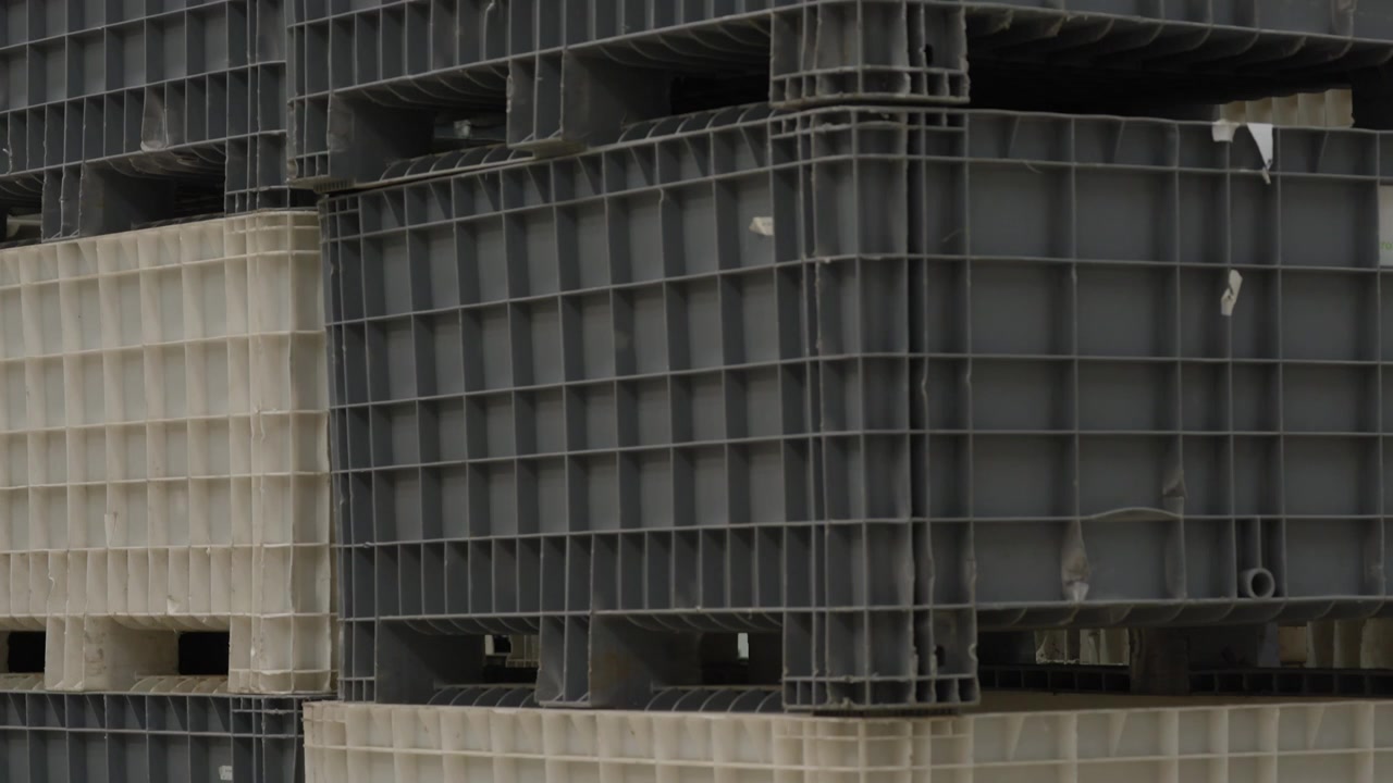 Stacked heavy duty plastic pallets in gray and beige piled high at industrial storage yard