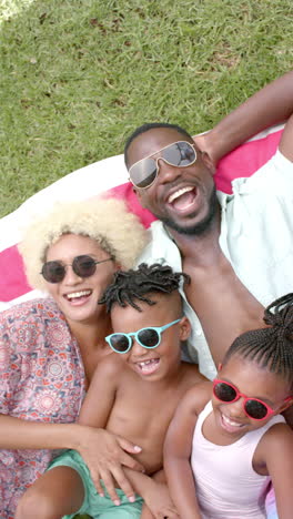 vertical video: african american family relaxing on grass, wearing sunglasses and smiling together