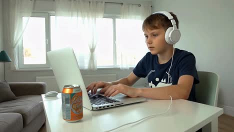 young boy with headphones studying online on laptop at home