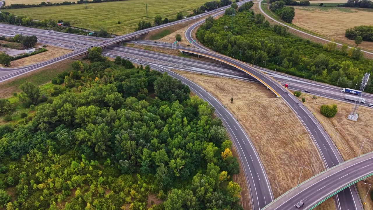 Traffic moves on highways near green fields and trees
