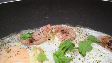 deslizándose a través de huevos fritos sazonados con pimienta y sal junto con salchicha y cebolla en una sartén caliente