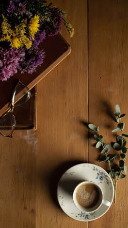 cozy flat lay of coffee, books, and flowers on a wooden table