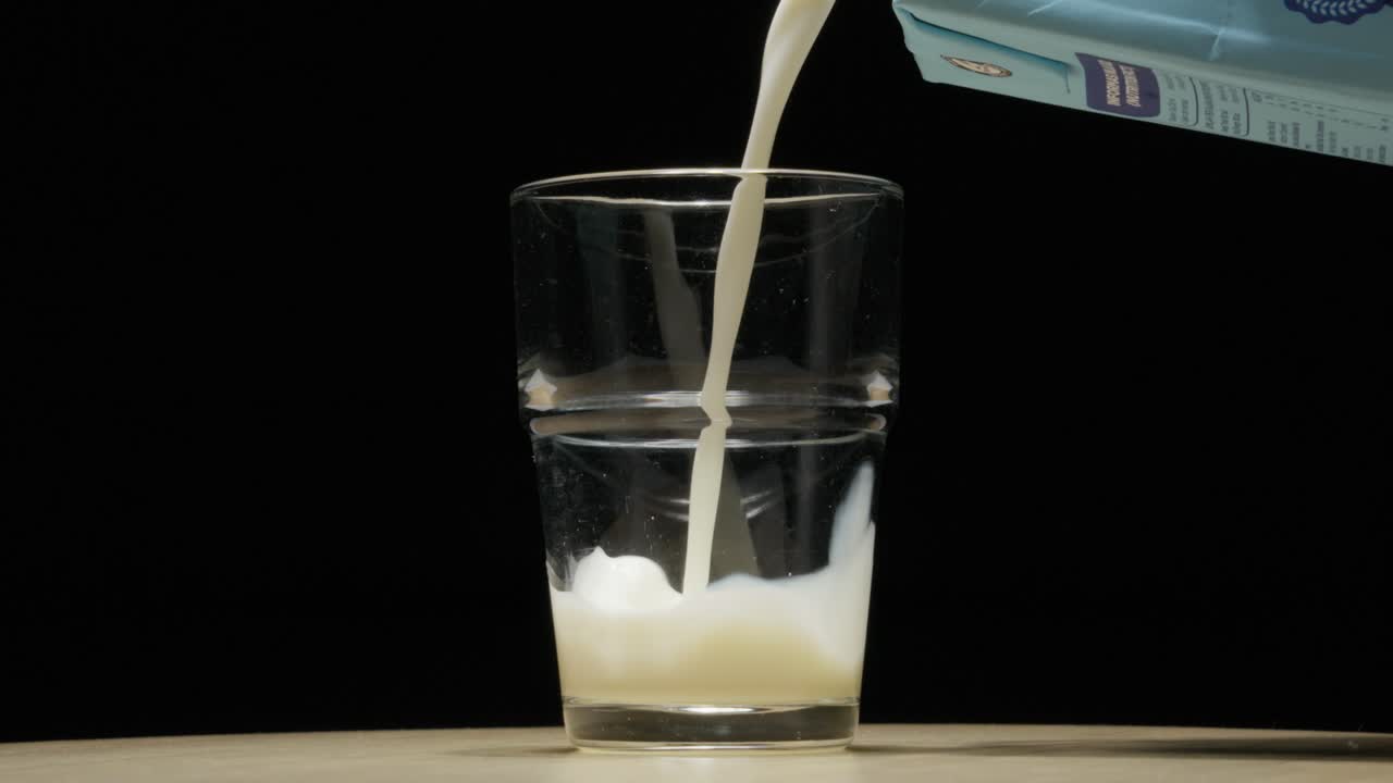 la leche se vierte en un vaso transparente, creando una salpicadura, contra un fondo oscuro
