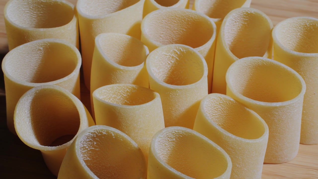 Primo piano di pasta tubolare secca su una superficie di legno con luce mutevole