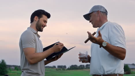 Two-men-talking-golf-course-outside.-Golfers-analyze-game-result-at-sunset-field