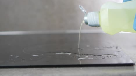 closeup of a hand pouring dish soap on a glass top stove