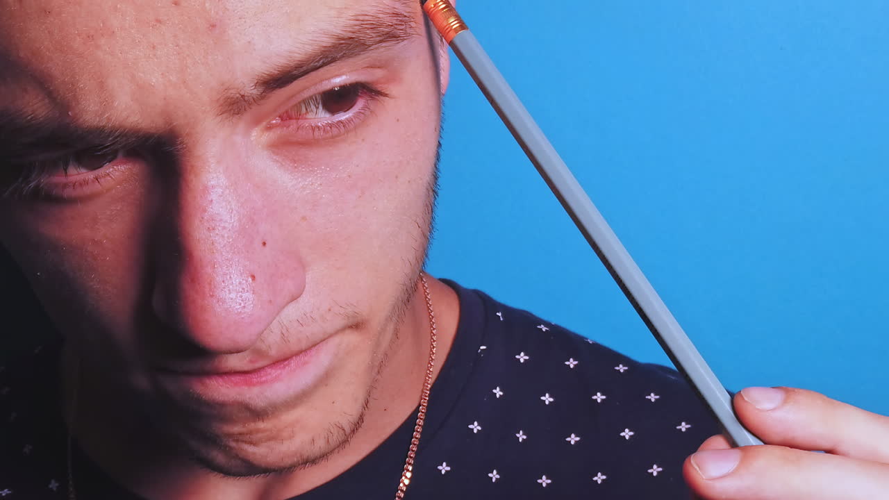 Close-up slow motion of thinking man with a pencil in front of a blue background
