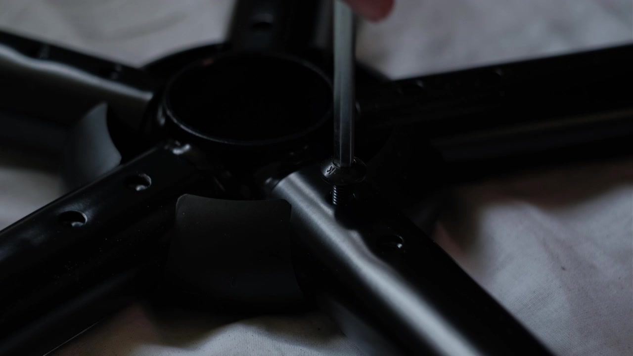 Close-up de mãos usando uma chave Allen para apertar um parafuso na base de uma cadeira de metal durante a montagem de móveis internos.