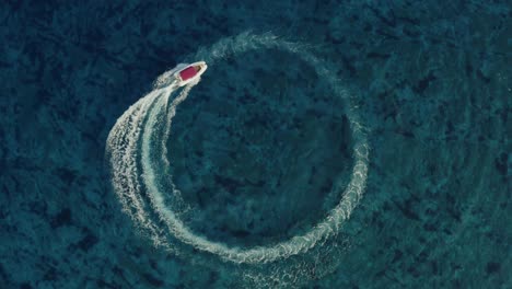 aerial shot of a fast speedboat with a red roof top going around in the circle and making beautiful doughnuts in the ocean