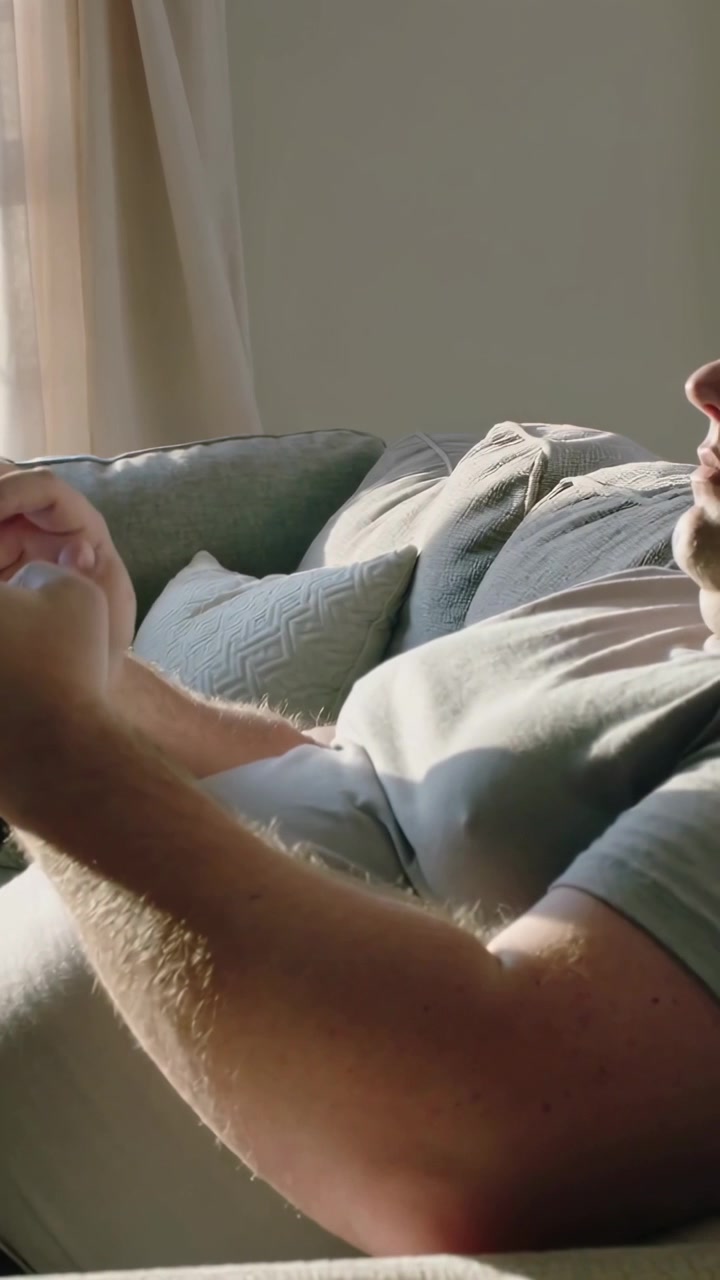 Video verticale: Uomo sdraiato che tiene lo smartphone, scorre sul divano vicino alla finestra, riposando.