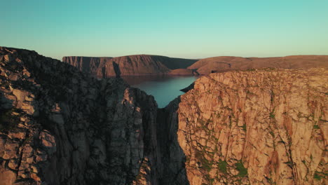 Drone-Acercándose-A-Un-Agujero-De-Acantilado-En-La-Costa-En-Un-Hermoso-Ambiente-De-Puesta-De-Sol-En-El-Norte-De-Noruega,-Paisaje-De-Acantilado-Noruego,-Cabo-Norte,-Escandinavia