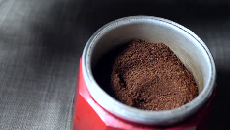 slow motion of an aluminum spoon filling up the middle compartment of a red italian coffee maker with coffee powder while leveling it