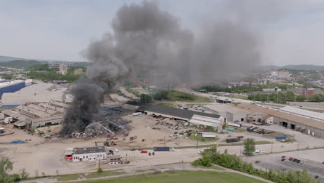 Wide-aerial-static-footage-of-a-large-industrial-fire-with-firefighters-fighting-it-with-a-highway-in-the-background-in-Chattanooga,-TN