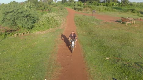 aerial shot tracking from the front a ginger haired bearded explorer riding on a african rural dirt road on a motor cycle